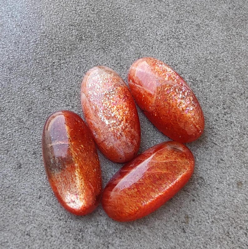 K&ouml;nnte beinhalten: Vier ovale Cabochons aus Sunstone in Orange- und Rott&ouml;nen mit schimmerndem, irisierendem Finish.