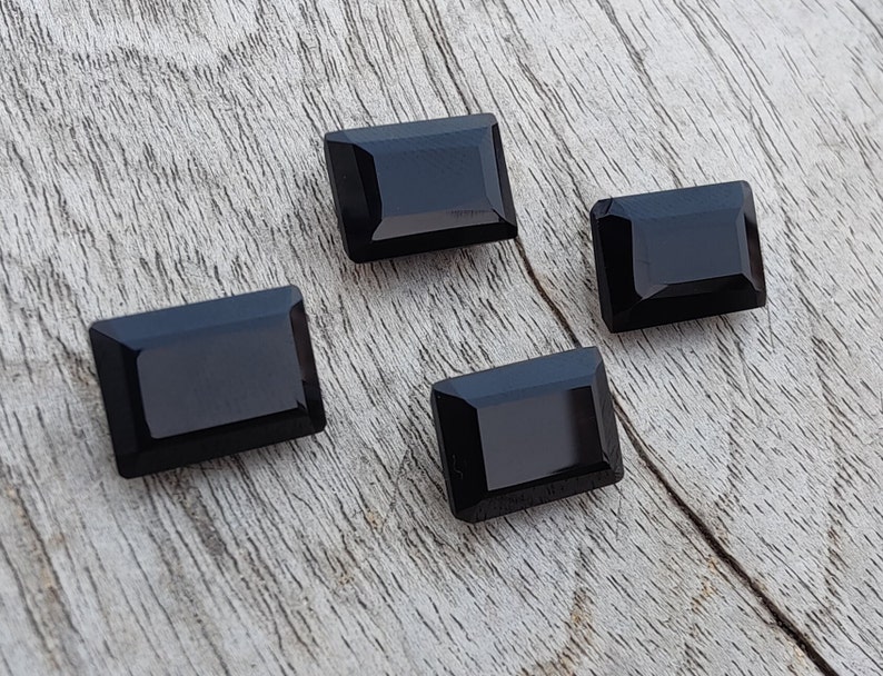 Pu&ograve; includere: Quattro pietre preziose rettangolari nere con finitura lucida. Le pietre preziose sono disposte su una superficie di legno marrone chiaro.