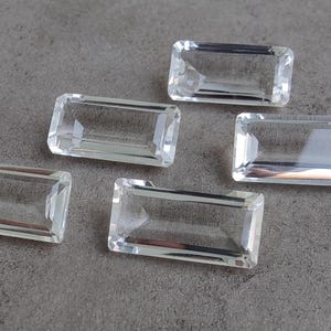 Może przedstawiać: Pięć przezroczystych, prostokątnych, fasetowanych kamieni szlachetnych. Kamienie szlachetne są ułożone w rzędzie na szarej powierzchni.