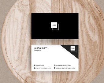 Könnte beinhalten: Zwei schwarz-weiße Visitenkarten auf einer Holzoberfläche. Die obere Karte hat einen schwarzen Hintergrund mit einem weißen quadratischen Logo. Die untere Karte hat einen weißen Hintergrund mit einem schwarzen quadratischen Logo und dem Text "JASON SMITH, OWNER".