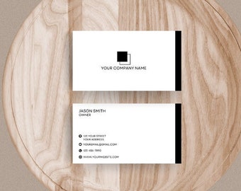 Könnte beinhalten: Zwei weiße Visitenkarten mit schwarzen Rändern auf einer Holzoberfläche. Die obere Karte hat ein schwarzes Quadrat mit dem Text "YOUR COMPANY NAME". Die untere Karte hat den Text "JASON SMITH - DESIGNER" und Kontaktinformationen.