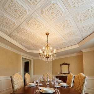 May include: A dining room featuring a coffered ceiling with white and gold embossed square tiles. A multi-tiered brass chandelier with crystal accents hangs above a dark wood table set with white plates, clear glassware, and silver cutlery.