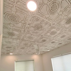 May include: White ceiling with a decorative pattern of brown squares and circles. A white ceiling fan is in the center of the image.