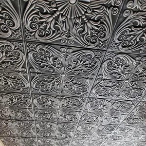 May include: A black and white ceiling tile with a decorative, ornate, floral pattern.