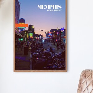 Pode incluir: Uma fotografia emoldurada de uma cena de rua em Memphis, Tennessee. A imagem mostra uma rua ladeada por edifícios, com letreiros de néon e postes de luz. O texto "MEMPHIS BEALE STREET" está impresso no topo da imagem. Há motocicletas estacionadas ao lado da rua.