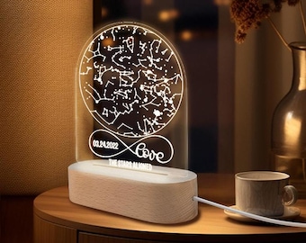 Puede incluir: Una luz nocturna LED blanca con una base de madera. La luz presenta un mapa de constelaciones con la fecha "03.24.2022" y la palabra "Love" con el texto "The Stars Aligned" debajo.