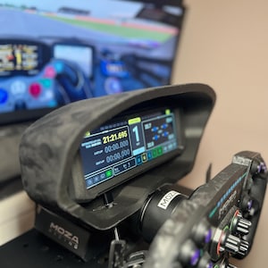 Puede incluir: Un salpicadero negro de simulador de carreras con una pantalla digital que muestra los tiempos por vuelta y otros datos de carrera. El salpicadero está montado en un volante con la marca "MOZA" visible. La pantalla muestra el número 1.