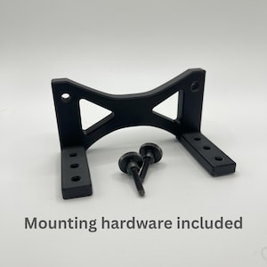 May include: Black metal mounting bracket with two black thumb screws. The bracket has a unique shape with triangular cutouts and multiple mounting holes. The text "Mounting hardware included" is visible below the bracket.