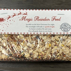 May include: A clear plastic bag filled with a mixture of grains and seeds, labeled "Magic Reindeer Food." The label features a Santa and sleigh graphic and text that reads, "Sprinkle on the lawn Christmas Eve night."