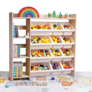 May include: A wooden toy organizer with multiple storage bins filled with colorful balls and toys. The top shelf displays a wooden rainbow and miniature trees. Books are stored on the side shelves. The organizer sits on a colorful play mat.