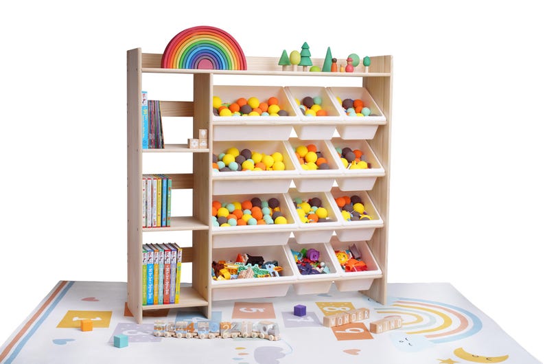 May include: A wooden toy organizer with multiple storage bins filled with colorful balls and toys. The top shelf displays a wooden rainbow and miniature trees. Books are stored on the side shelves. The organizer sits on a colorful play mat.