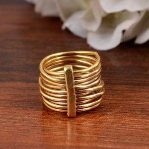 May include: A gold-toned ring with multiple bands stacked on top of each other. The bands are connected by a vertical bar in the center.