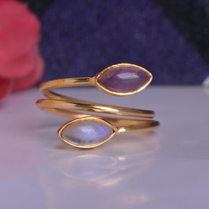 May include: A gold ring with two oval-shaped gemstones. The top stone is a purple amethyst and the bottom stone is a white moonstone.