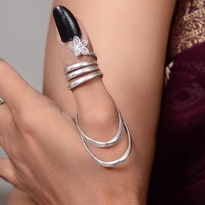 Könnte beinhalten: Ein silberner Daumenring mit einem zarten Blumendesign. Der Ring besteht aus mehreren Bändern, die sich um den Daumen wickeln.