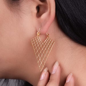 Puede incluir: Pendientes geométricos dorados con forma triangular y un patrón de diamantes.