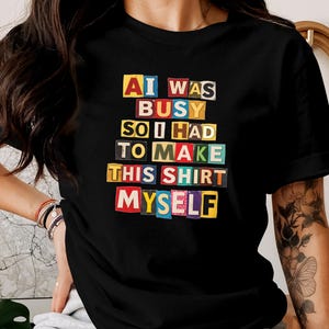 Pode incluir: T-shirt preto com o texto "AI WAS BUSY SO I HAD TO MAKE THIS SHIRT MYSELF" em um estilo de letras recortadas coloridas. A camisa tem mangas curtas e decote redondo. O texto está disposto em formato empilhado.