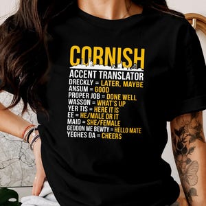 May include: Black t-shirt featuring the text "CORNISH ACCENT TRANSLATOR" in yellow, with a list of Cornish phrases and their English meanings. The shirt is a crew neck with short sleeves.