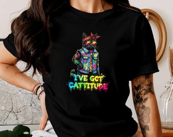 Könnte beinhalten: Schwarzes T-Shirt mit einer Cartoon-Katze, die eine Sonnenbrille, ein rotes Bandana und eine Jeansjacke mit bunten Akzenten trägt. Der Text "I'VE GOT CATTITUDE" wird in einer lebendigen, mehrfarbigen Schrift angezeigt.