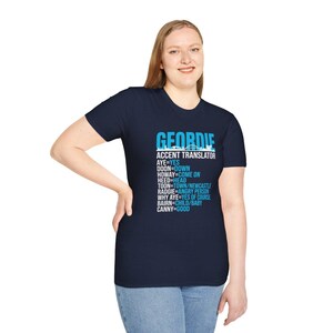 Puede incluir: Camiseta azul marino con la palabra "GEORDIE" en azul claro y el texto "ACCENT TRANSLATOR" debajo. La camiseta presenta una lista de t&eacute;rminos de jerga Geordie y sus traducciones al ingl&eacute;s.