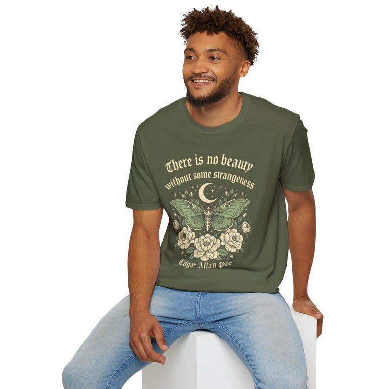 May include: Olive green t-shirt featuring a graphic of a moth with a crescent moon and floral elements. The text "There is no beauty without some strangeness" and "Edgar Allan Poe" are also printed on the shirt.