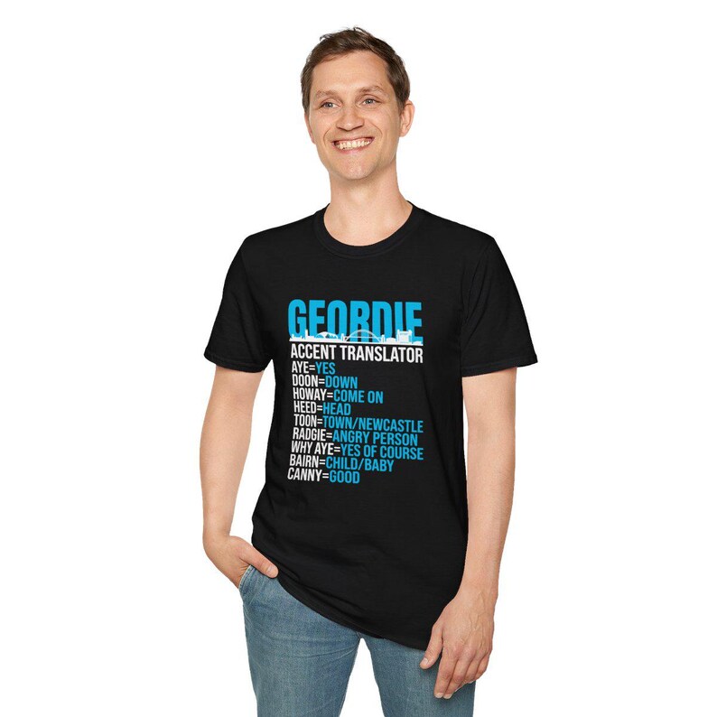 Puede incluir: Camiseta negra con el texto "GEORDIE ACCENT TRANSLATOR" en blanco y azul. La camiseta enumera t&eacute;rminos de jerga Geordie y sus traducciones al ingl&eacute;s. La persona de la imagen lleva vaqueros azules.