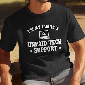 Puede incluir: Camiseta negra con texto blanco: "I'M MY FAMILY'S UNPAID TECH SUPPORT" y un gráfico de portátil. La camiseta de manga corta tiene cuello redondo. El texto está centrado en la parte delantera.