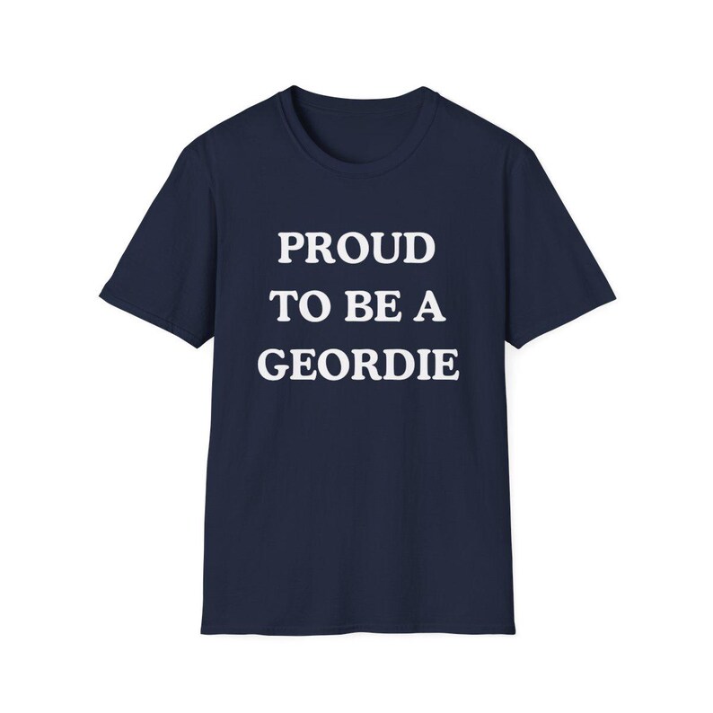 May include: A navy blue short-sleeved t-shirt featuring the white text PROUD TO BE A GEORDIE printed in a bold, sans-serif font across the center of the chest. The garment has a classic crew neckline and a straight hemline design.
