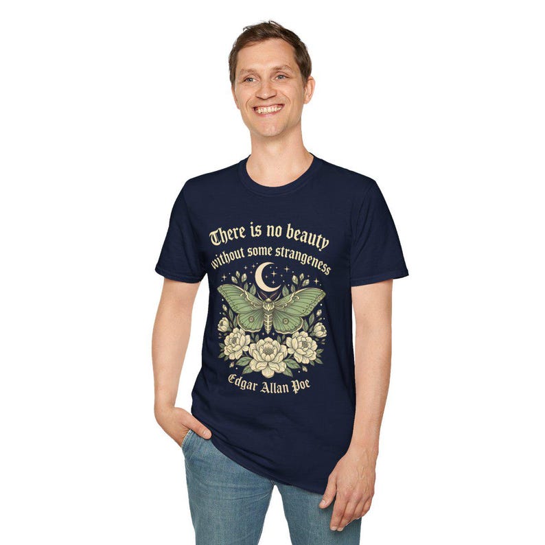 May include: Navy blue t-shirt featuring a green moth design with a crescent moon and floral accents. The shirt includes the quote "There is no beauty without some strangeness" by Edgar Allan Poe.