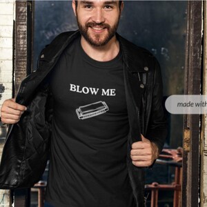 May include: A black t-shirt with the text "BLOW ME" and a harmonica graphic printed on the front.