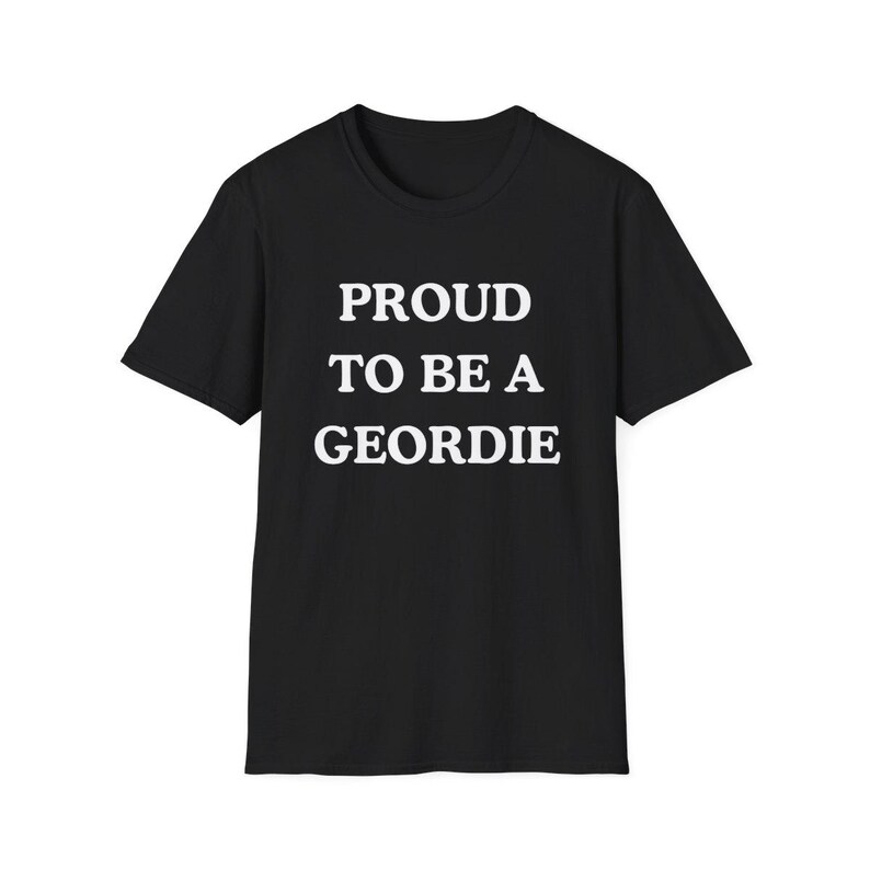 May include: A black short-sleeved t-shirt featuring the white text PROUD TO BE A GEORDIE centered on the chest. The garment has a crew neckline and a standard fit, constructed from a solid black fabric with bold, capitalized white lettering.