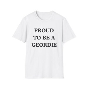 May include: A white short-sleeved t-shirt featuring the black text PROUD TO BE A GEORDIE centered on the chest. The garment has a classic crew neckline and a straight hemline, constructed from a plain white fabric with a simple, clean design.