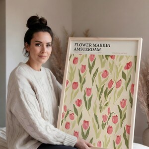 Woman sitting casually on the floor holding a large framed pastel botanical Amsterdam poster to show scale.