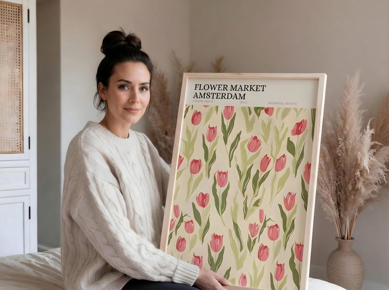 Woman sitting casually on the floor holding a large framed pastel botanical Amsterdam poster to show scale.
