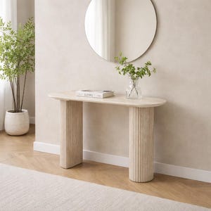 Puede incluir: Una mesa consola de color beige con una superficie lisa de forma ovalada, sostenida por dos columnas cilíndricas gruesas y estriadas. La mesa está fabricada en piedra texturizada y se asienta sobre un suelo claro, mostrando un diseño limpio.