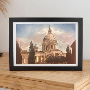 Può includere: Un dipinto ad acquerello incorniciato che raffigura un edificio classico con cupola e dettagli architettonici, circondato da cipressi verde scuro sotto un cielo azzurro e rosa tenue. L'opera è racchiusa in una semplice cornice nera.