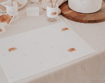 May include: A white placemat with a brown border and a light brown background. The placemat has a simple design with small brown pig illustrations scattered across the surface. The placemat is perfect for a rustic or farmhouse-themed table setting.