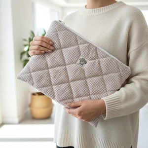 May include: A quilted zippered pouch featuring a beige and white gingham check pattern. The rectangular bag has a diamond-stitched texture and a small white fabric label in the center with the text Golden Yarn and a graphic of a ball of yarn.