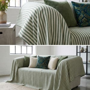May include: A sofa draped with a green and white striped throw blanket. The sofa is adorned with several throw pillows in shades of green, cream, and teal. The room has a neutral color palette with a rug and a vase of flowers.