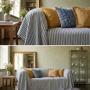 May include: A living room scene featuring a sofa draped with a blue and white striped throw. The sofa is adorned with mustard yellow, patterned blue, and fringed tan pillows. A gold-framed mirror and wooden side table with a vase of flowers are also present.
