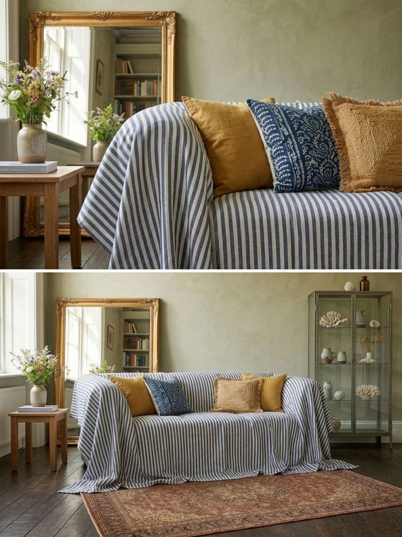 May include: A living room scene featuring a sofa draped with a blue and white striped throw. The sofa is adorned with mustard yellow, patterned blue, and fringed tan pillows. A gold-framed mirror and wooden side table with a vase of flowers are also present.