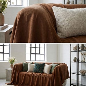 May include: A brown sofa draped with a matching throw blanket. Several decorative pillows in shades of green, white, and patterned blue are arranged on the sofa. A neutral rug and a black metal shelf unit are also visible.
