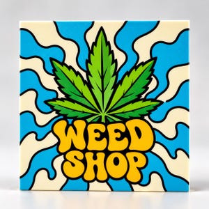 Op de afbeelding: Een vierkante keramische tegel met een centrale groene cannabisblad-afbeelding. Onder het blad staat de tekst WEED SHOP in dikke, gele, afgeronde letters. De achtergrond bestaat uit golvende, lichtblauwe en crèmekleurige strepen.