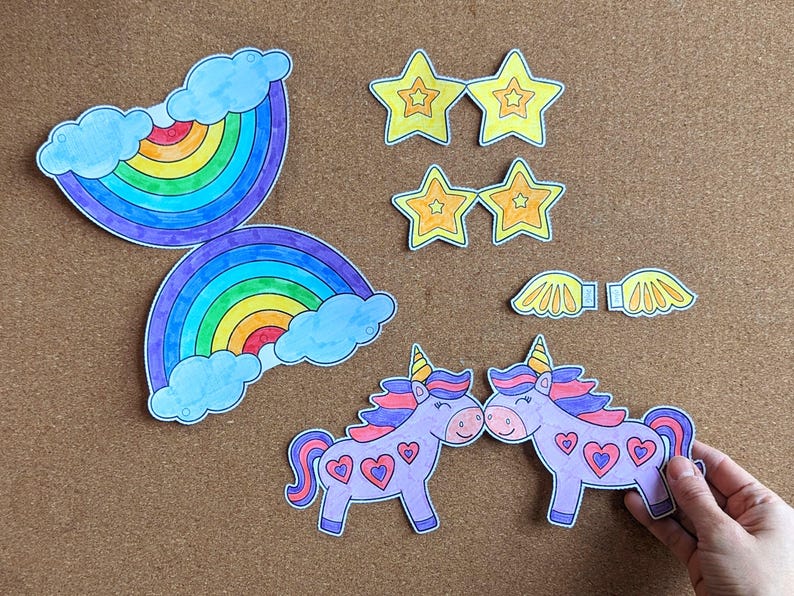 May include: Paper cutouts of rainbows, stars, wings, and unicorns. The unicorns are purple with pink manes and heart details. The stars are yellow with orange outlines. The rainbows have blue clouds.