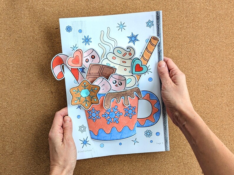 Peut inclure: Illustration color&eacute;e d'une tasse de chocolat chaud avec des guimauves, une canne en sucre et un biscuit pain d'&eacute;pices. La tasse est d&eacute;cor&eacute;e de flocons de neige et d'une anse bleue. L'image est tenue par deux mains.