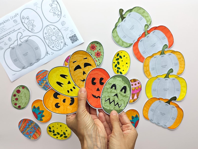 Op de afbeelding: Een verzameling papieren knutselwerkjes met diverse ovale vormen met kleurrijke patronen en pompoengezichten, naast verschillende pompoenvormige sjablonen en een instructieblad met de titel Pumpkins Craft en een QR-code.