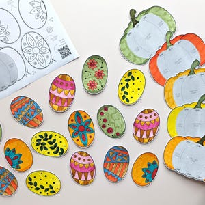 Op de afbeelding: Een papieren knutselset met gedrukte sjablonen voor pompoenen en ovale vormen. De set bevat een wit instructieblad met zwarte lijntekeningen en meerdere kleurrijke, met de hand uitgeknipte papieren ovalen en pompoenen met diverse patronen.