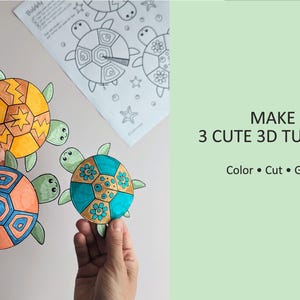Op de afbeelding: Drie kleurrijke 3D-schildpadknutsels met oranje, blauwe en gele schilden worden getoond, met een kleurplaat op de achtergrond. De tekst luidt "MAKE 3 CUTE 3D TURTLES" met de instructies "Color &bull; Cut &bull; Glue".