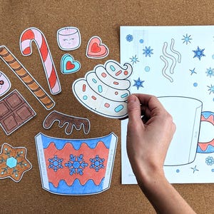 Peut inclure: Divers &eacute;l&eacute;ments en papier d&eacute;coup&eacute; pour un projet de bricolage sur le th&egrave;me de l'hiver. Comprend une tasse, de la cr&egrave;me fouett&eacute;e, des guimauves, une canne en sucre, du chocolat et des flocons de neige. Sur une surface marron.