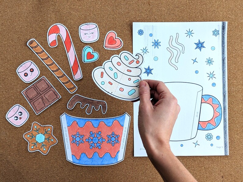 Peut inclure: Divers &eacute;l&eacute;ments en papier d&eacute;coup&eacute; pour un projet de bricolage sur le th&egrave;me de l'hiver. Comprend une tasse, de la cr&egrave;me fouett&eacute;e, des guimauves, une canne en sucre, du chocolat et des flocons de neige. Sur une surface marron.