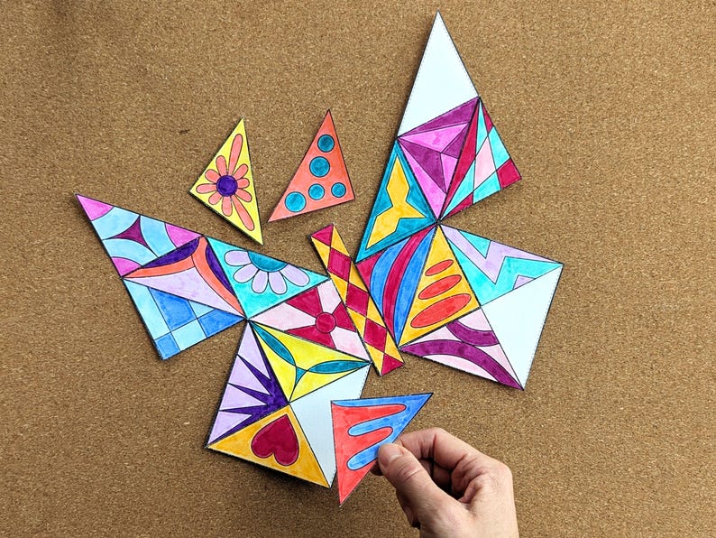 May include: A colorful butterfly puzzle made of triangular pieces. The puzzle pieces are decorated with various patterns and colors, including pink, blue, yellow, and red. A hand is holding one of the puzzle pieces.